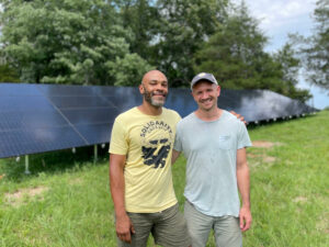 two men smiling in foreground with solar ground mount array in background